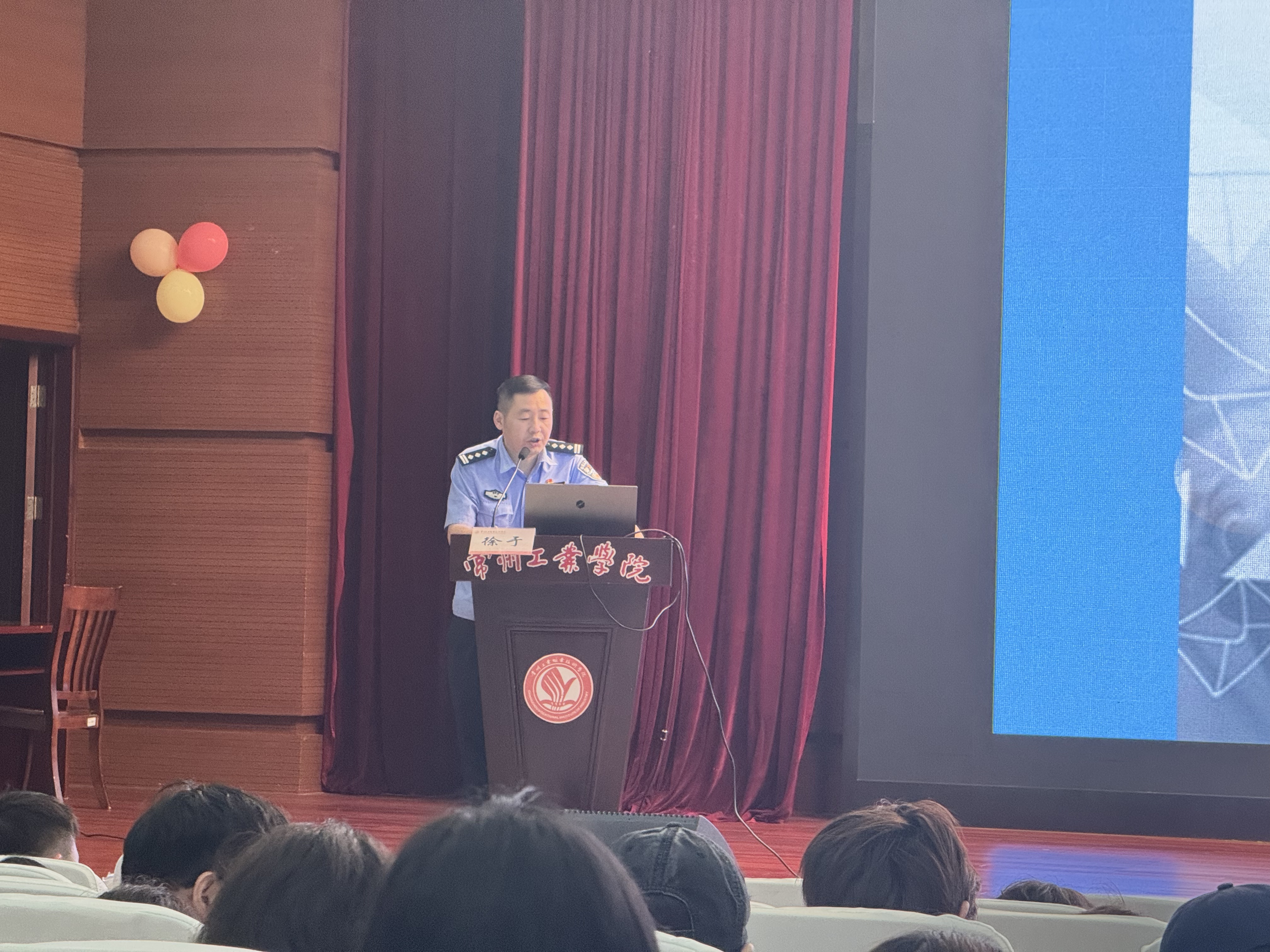 【图片2】讲座现场：警官在讲台讲解，台下学生专注听讲并记录